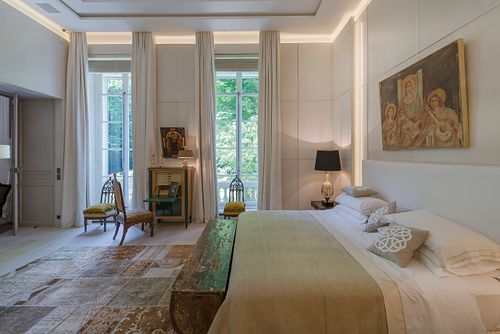 Chambre à coucher haussmannienne à Saint-Germain-des-Prés avec lit central, grande fenêtre donnant sur le jardin et mobilier élégant. Photographie d'architecture intérieure par Nicolas Karadimos.
