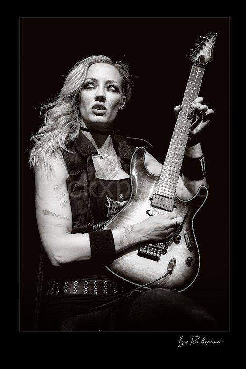 Vertical black and white image of Nita Strauss performing live on stage with an electric guitar in a close concert portrait