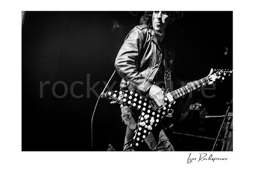 Horizontal black and white image of Brent Woods playing guitar on stage with a polka-dot V-shaped guitar