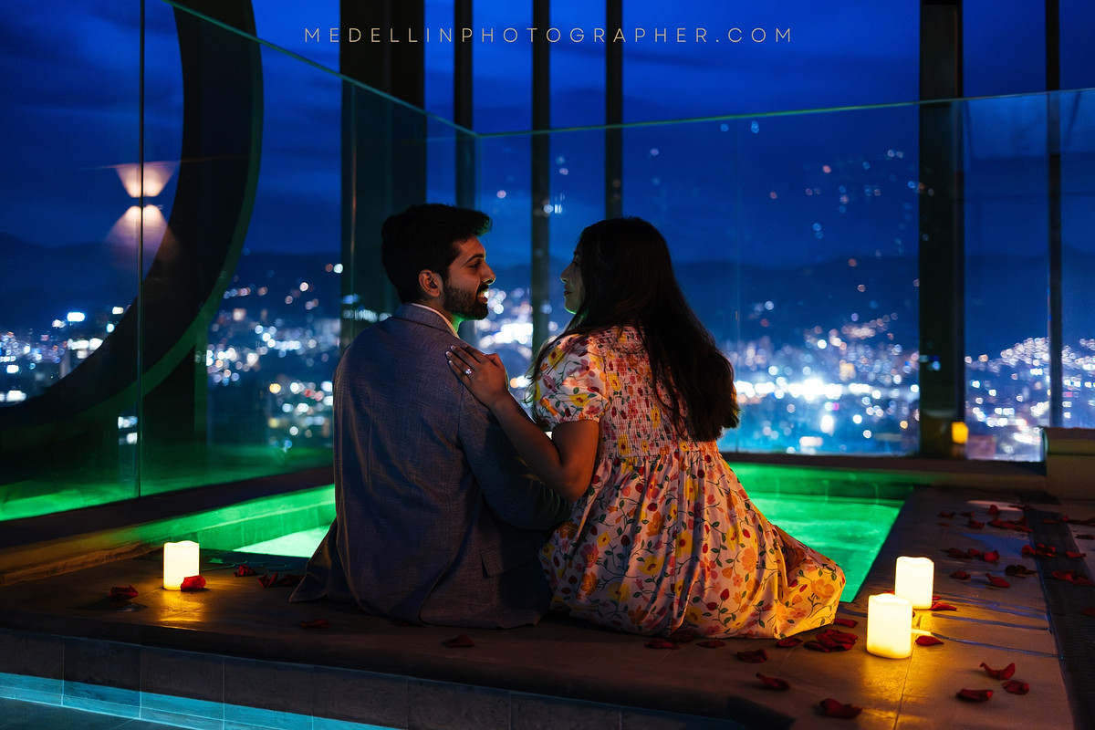 Couple sitting among candles on a rooftop terrace at blue hour above the Medellin city lights