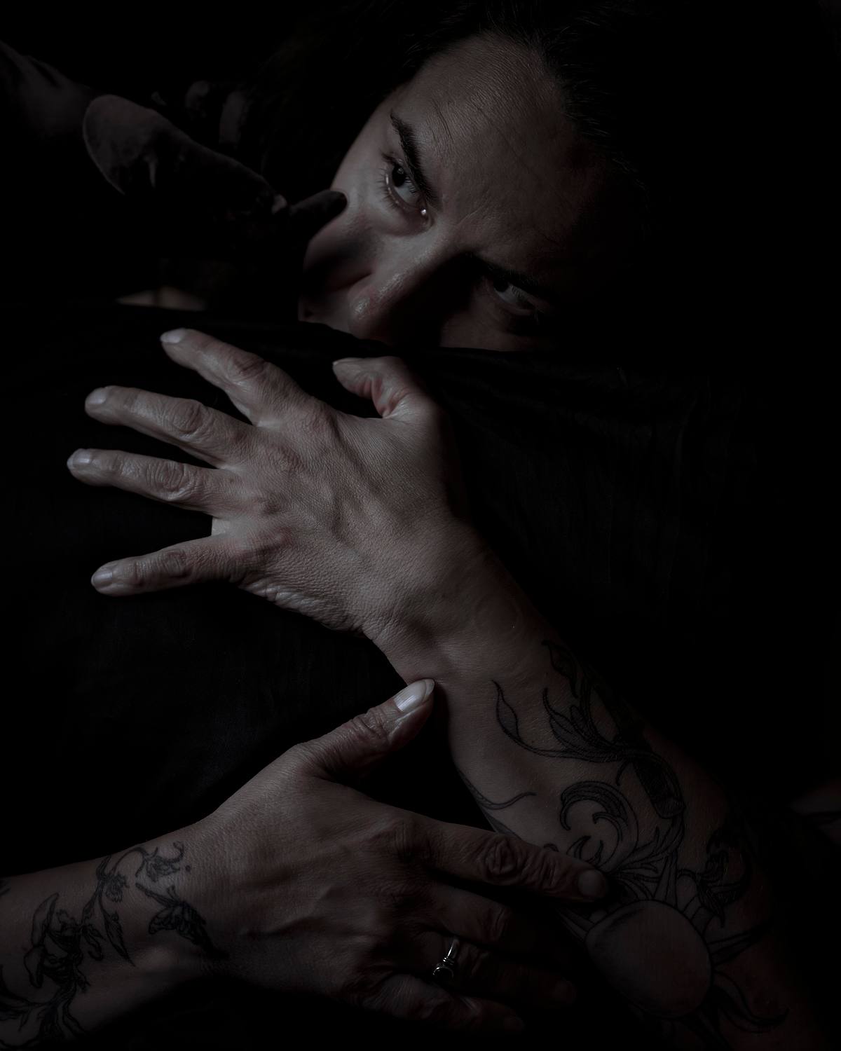 Self-portrait embracing black form while shadow hand touches face.