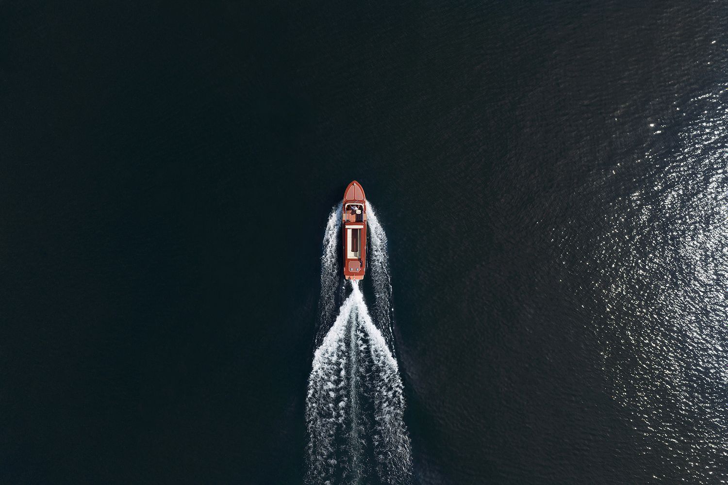 Wooden Venetian style taxi boat navigating Lake Como seen from a drone