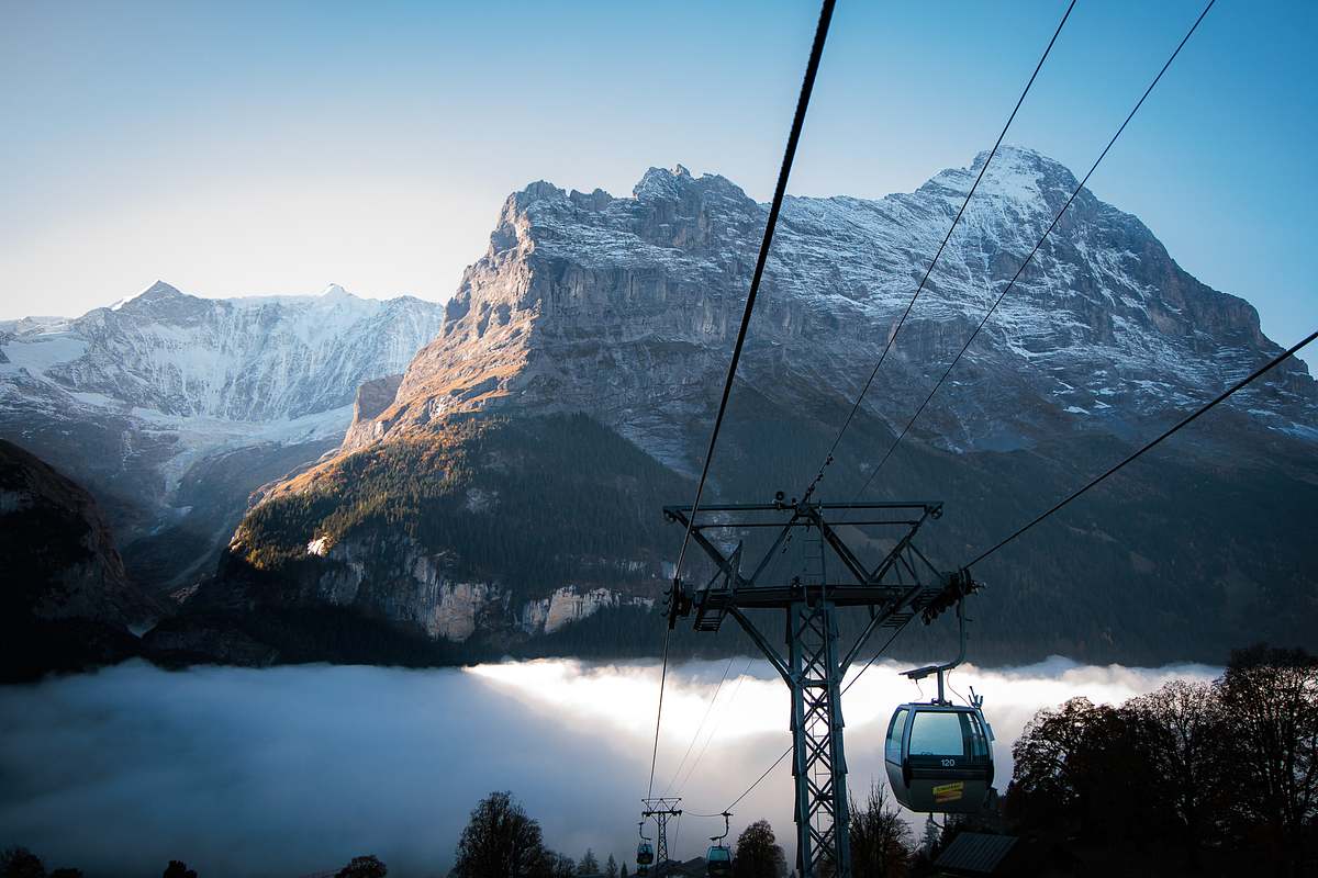 Gondelbahn mit Kabine Nummer 120 schwebt &uuml;ber einem dichten Nebelmeer im Tal, dahinter schneebedeckte Gipfel und Tannensilhouetten im Gegenlicht