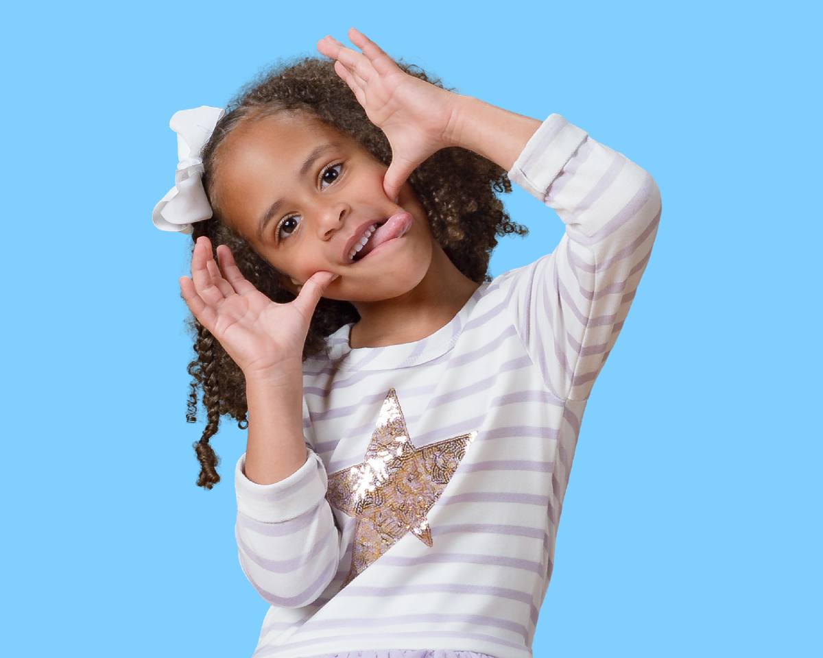 Preschool child posing making-playful-face wearing striped shirt and gold star on light blue background