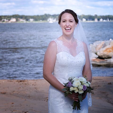 bride smiling and holding her flowers in the hand during a summer wedding with the Chesapeake bay in the backgrond