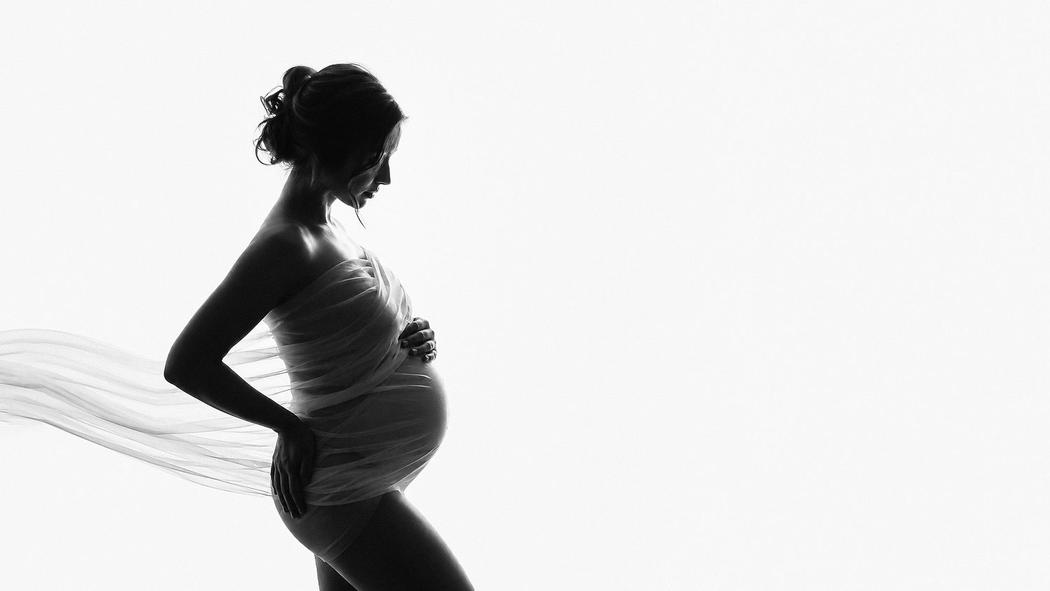 Black and white silhouette maternity studio portrait of a pregnant woman wrapped in flowing fabric on a white background in Tallinn