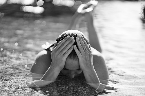 Jeune femme allongée sur la plage, le visage caché par ses mains en noir et blanc.