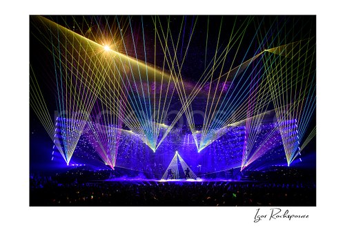 Horizontal color image of Trans Siberian Orchestra performing on stage beneath multicolored laser lights and a glowing concert backdrop