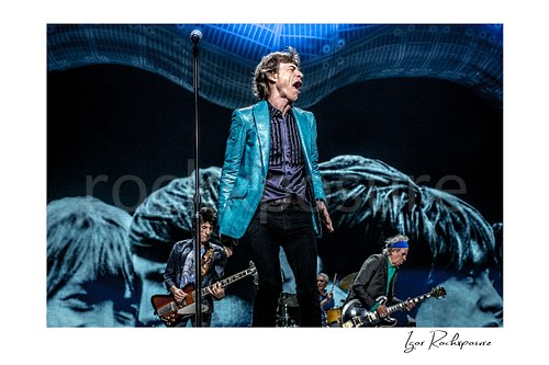 Horizontal color image of Mick Jagger, Ronnie Wood, Charlie Watts and Keith Richards of The Rolling Stones performing on stage beneath a vivid blue concert backdrop
