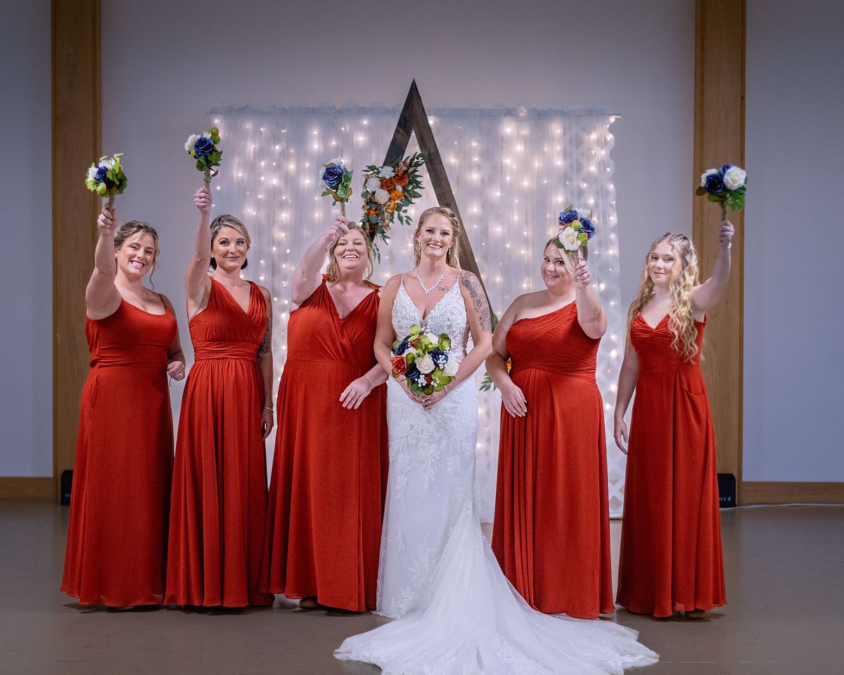 bride and her brides maid posing in front of arbor, bride is holding her flowers and the bridesmaids are raising their flowers in the air