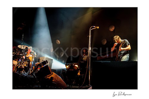 Horizontal color image of Dan Auerbach and Patrick Carney of The Black Keys performing live on stage under a dramatic spotlight