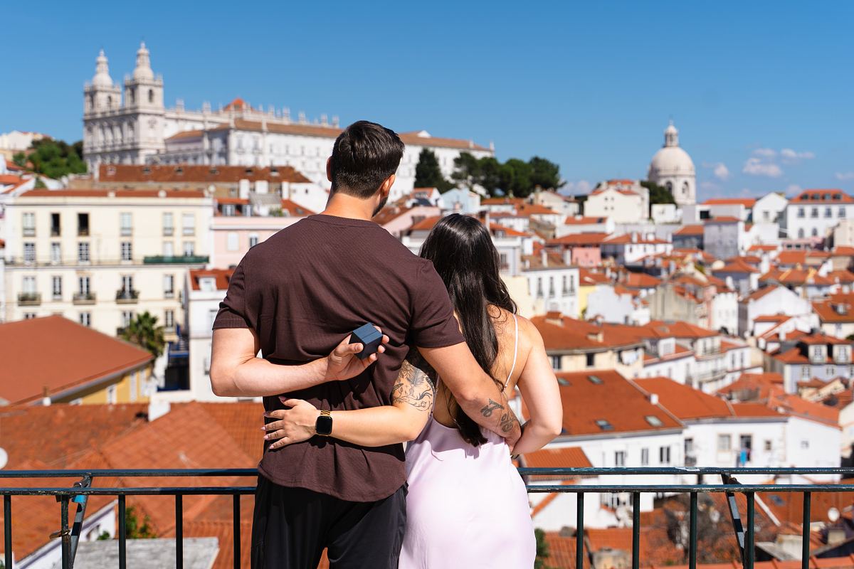 Man hiding an engagement ring behind his partner overlooking Alfama