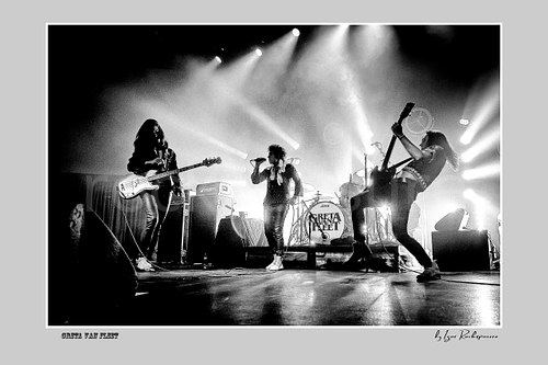 Horizontal black and white image of Greta Van Fleet performing on stage with Sam Kiszka on the left, Josh Kiszka in the center, and Jake Kiszka on the right