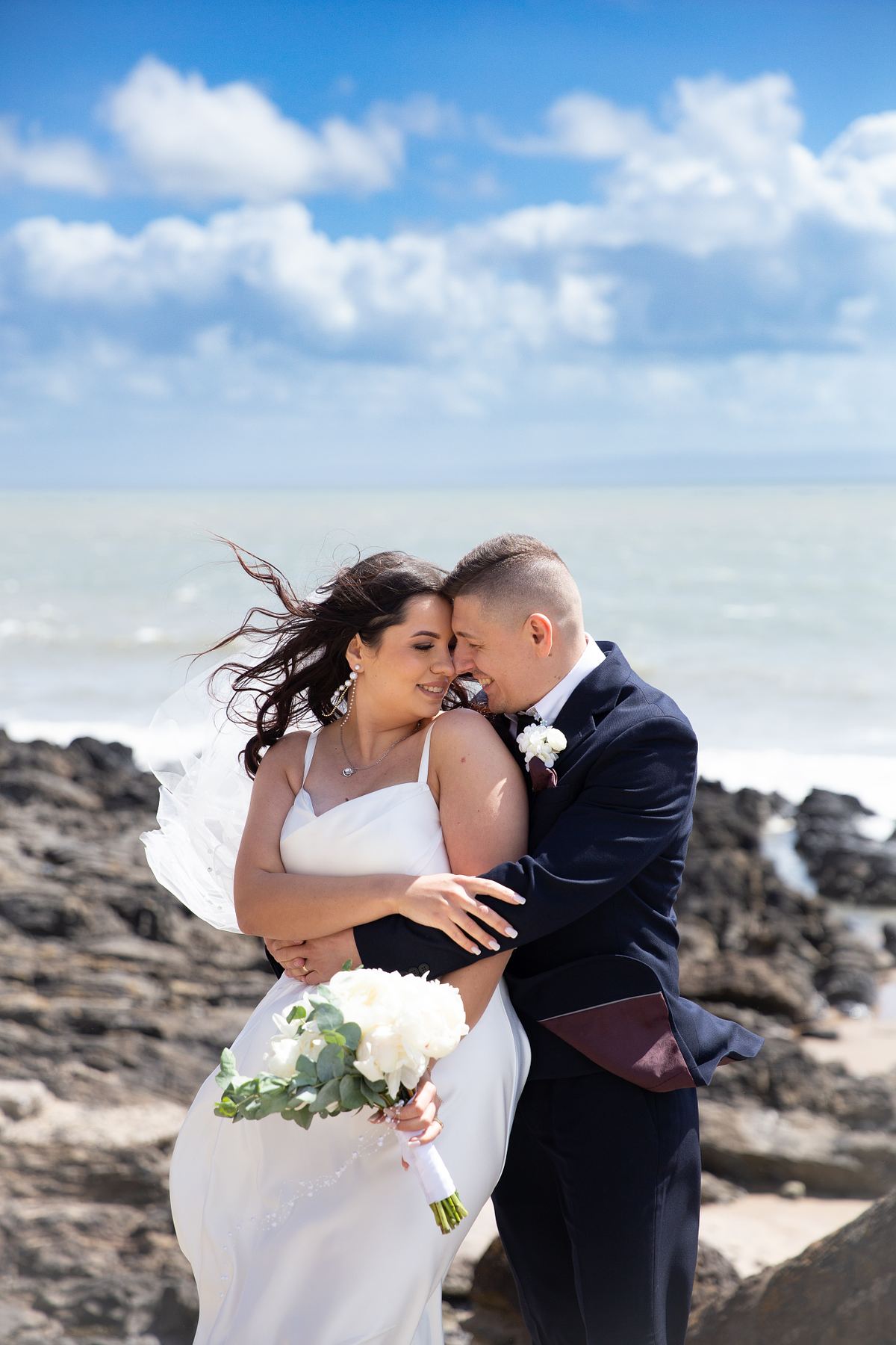 Bride and groom walking along the rocky coastline at Barry Island