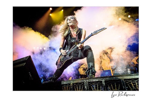 Horizontal color image of Nita Strauss performing live on stage with an electric guitar, surrounded by thick stage smoke and flying hair