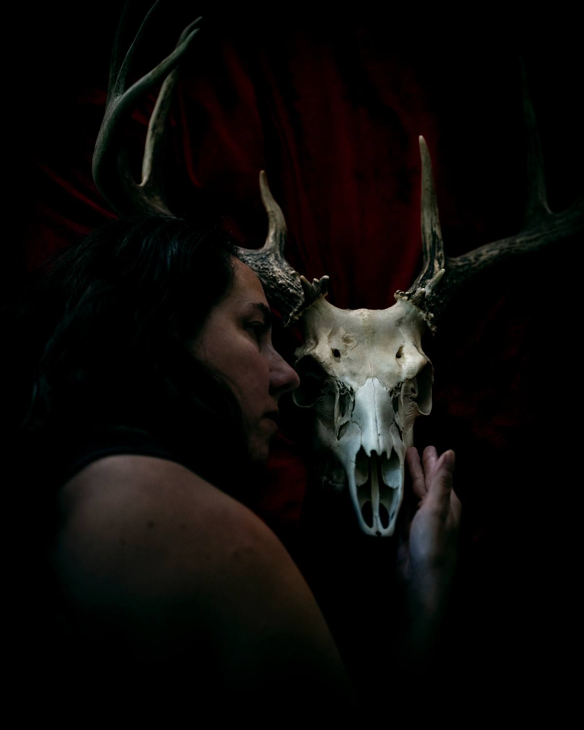 Self-portrait holding a deer skull against deep red fabric.