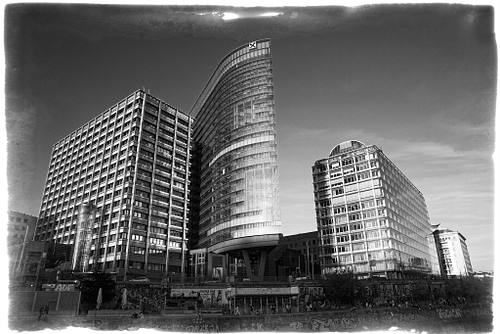 Schwarz-Weiß-Architekturfotografie am Wiener Donaukanal mit Blick auf das moderne Raiffeisen-Glashaus, den älteren Gebäudeteil links und den IBM-Block rechts an der Oberen Donaustraße, aufgenommen im Weitwinkel mit historischem Vintage-Rahmen.