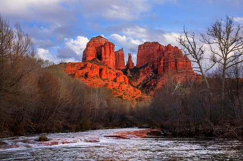 A dramatic horizontal fine art photograph of Castle Rock in Sedona, Arizona, captured at sunset with vibrant golden hour light illuminating the red rock formation.