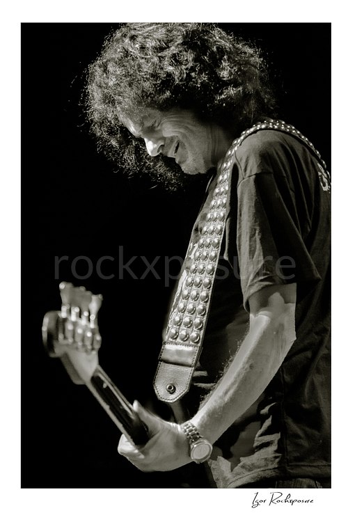 Vertical black and white image of Jimmy Bain of Last in Line playing bass onstage in a quiet live performance portrait
