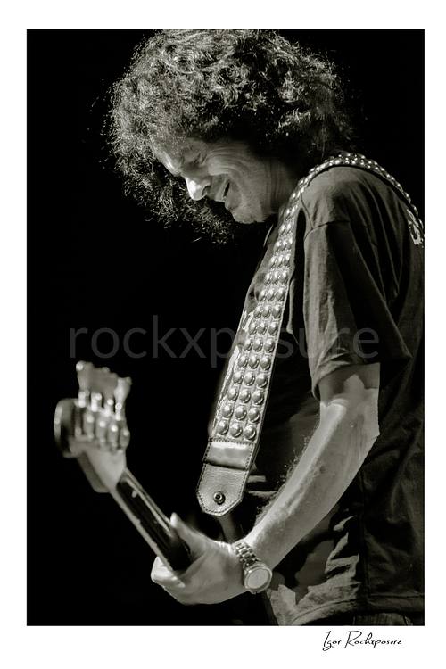 Vertical black and white image of Jimmy Bain of Last in Line playing bass onstage in a quiet live performance portrait