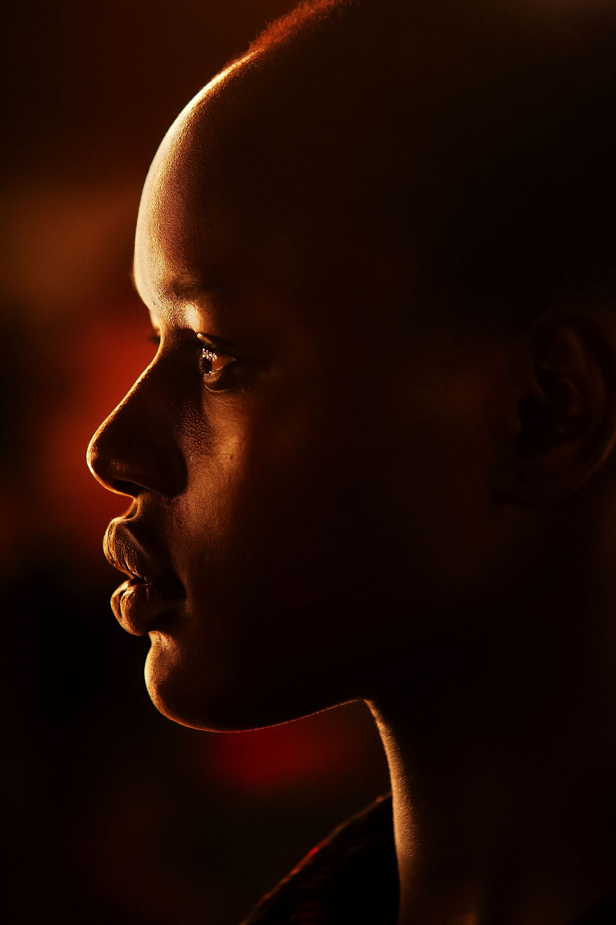 Dark skinned fashion model photographed from profile on dark background.