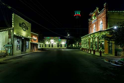 A horizontal fine art color night photograph of the main street in historic Gruene, Texas, illuminated by green and white Christmas lights with Gruene Hall and the water tower in the background.