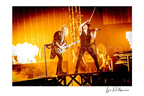 Horizontal color image of Chris Caffery and Roddy Chong of Trans Siberian Orchestra performing on stage with guitar, violin, and flames