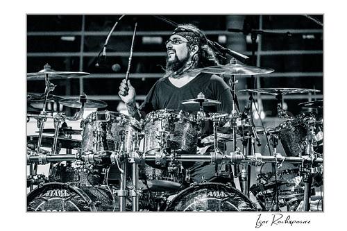 Horizontal black and white image of Mike Portnoy smiling at the drum kit during a live performance