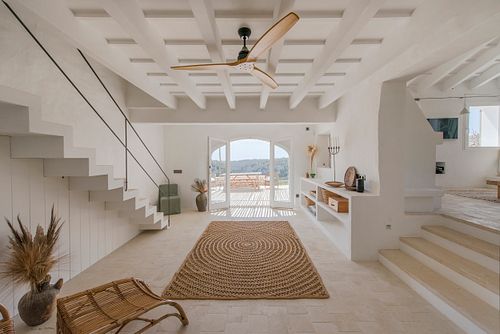 Salon lumineux avec plafond à caissons, escalier et grand tapis en jonc dans la finca Son Fonoll à Minorque. Photographie par Nicolas Karadimos.