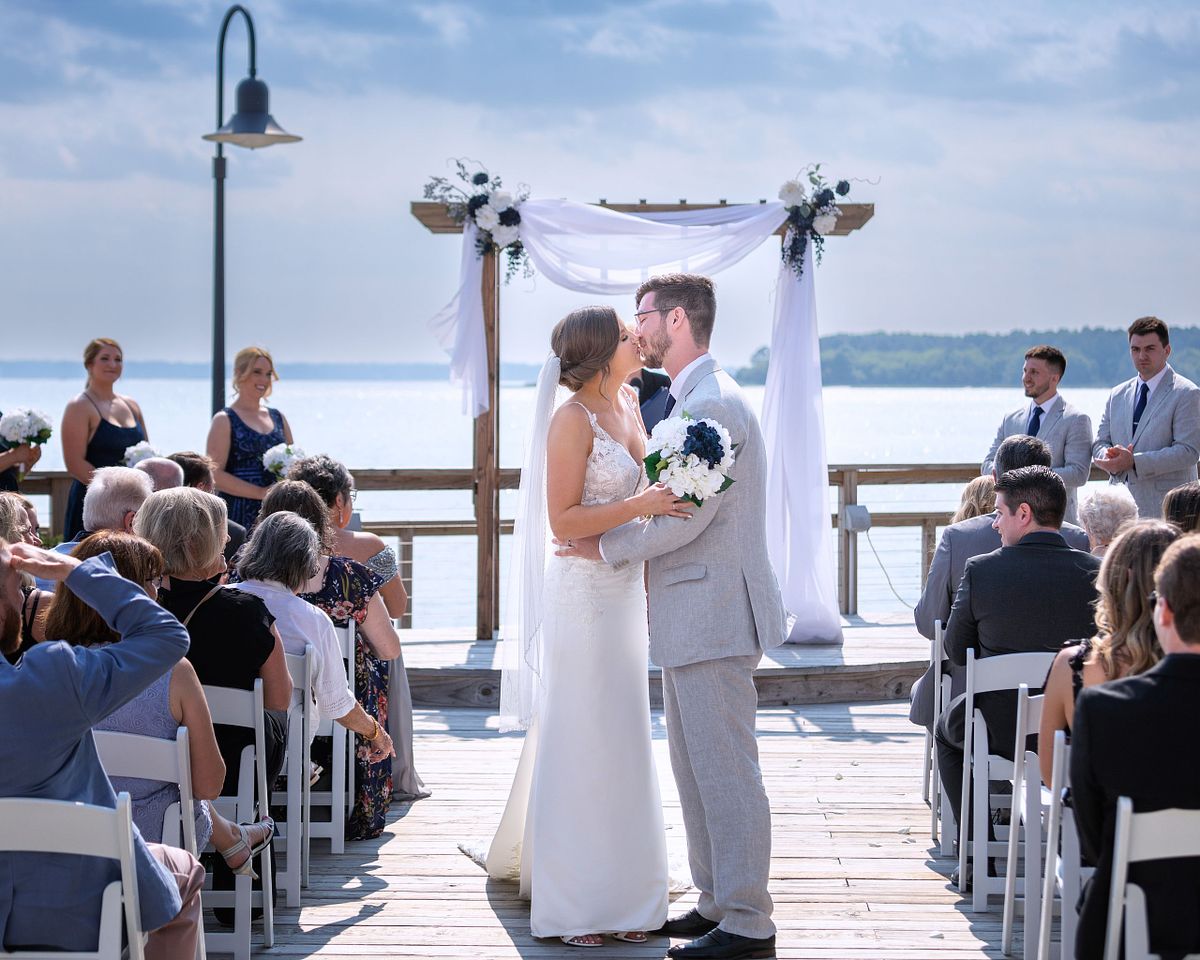 bride and groom kissing after the ceremony in the aisle with the wedding arbor and rehoboth beach in the background