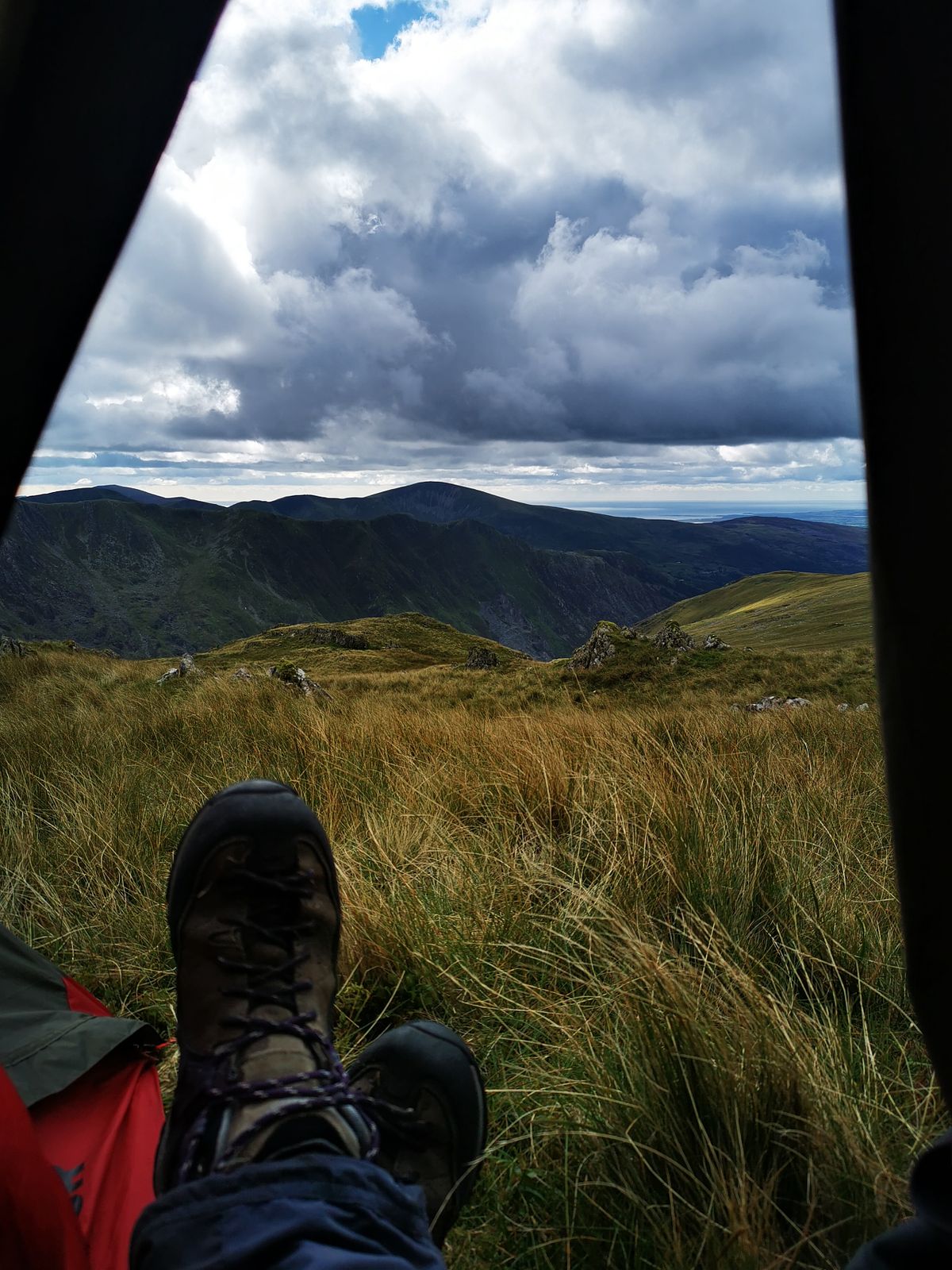 View from a tent overlooking the mountains of Wales with rolling clouds and hiking boots in the foreground.