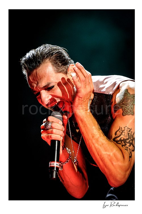 Vertical color image of Depeche Mode singer Dave Gahan singing into a microphone during a live performance