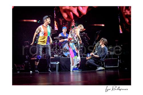 Horizontal color image of Anthony Kiedis, Chad Smith, Flea, and Josh Klinghoffer of Red Hot Chili Peppers performing live on stage, with Smith at the drum kit while the band gathers in a dynamic full-band concert moment